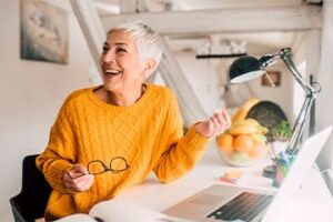 Foto de senhora com cabelos grisalhos sorrindo no seu escritório.