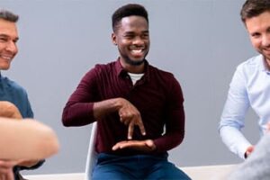 Foto de homem negro sentado fazendo com as mãos e dois dedos uma representação de caminhar.