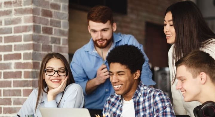 Foto de três homens e duas mulheres em frente a um notebook.