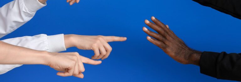 Foto com mãos brancas apontando para mãos negras, representando a xenofobia e racismo.