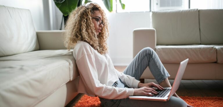 Mulher negra sentada no tapete vermelho da sala de casa encostada no sofá branco, preenchendo pesquisa Percepções sobre profissionais neurodivergentes. #Neurodivergentes #Autismo #TDAH #Dislexia